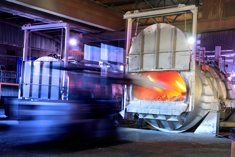 Two large industrial kilns with one hatch open and the material being fed in as a blur