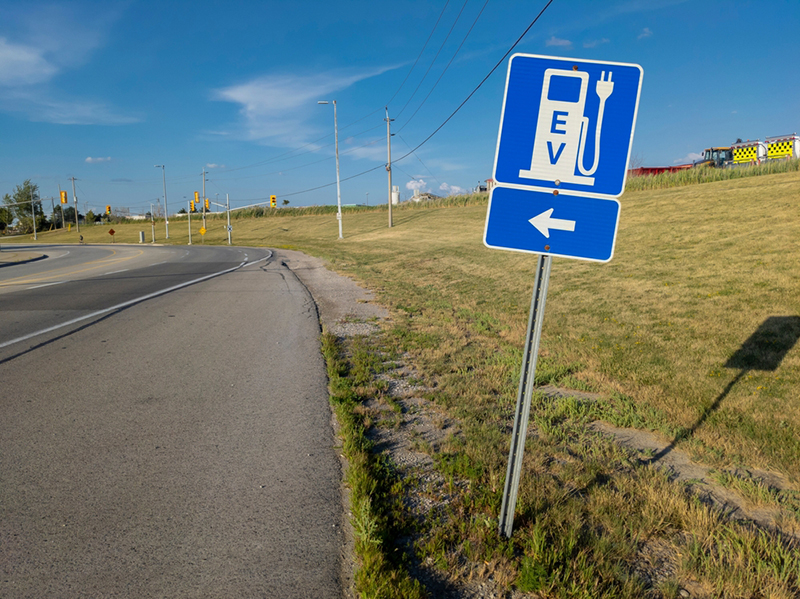 Road sign EV with direction arrow for the electrical vehicle chargers. New technology, green power, zero emission and carbon footprint transportation concept.