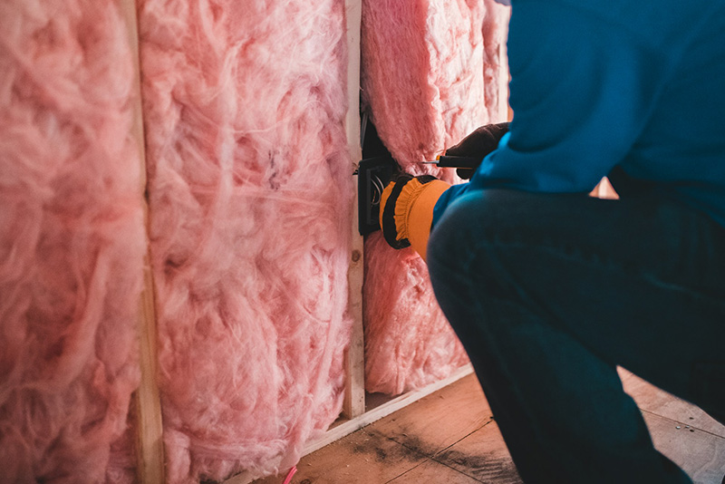 A person in blue clothing installing insulation between wood slats