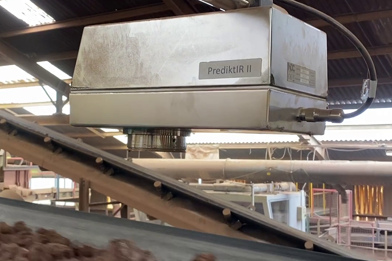 Metal box suspended from ceiling above angled conveyor belt in a factory