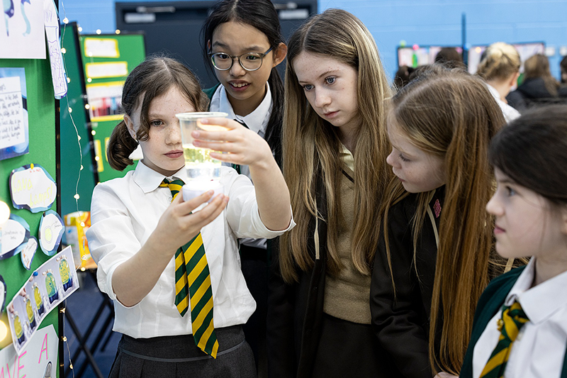 Image of five schoolchildren gathered around a plastic cup containing chemical solution