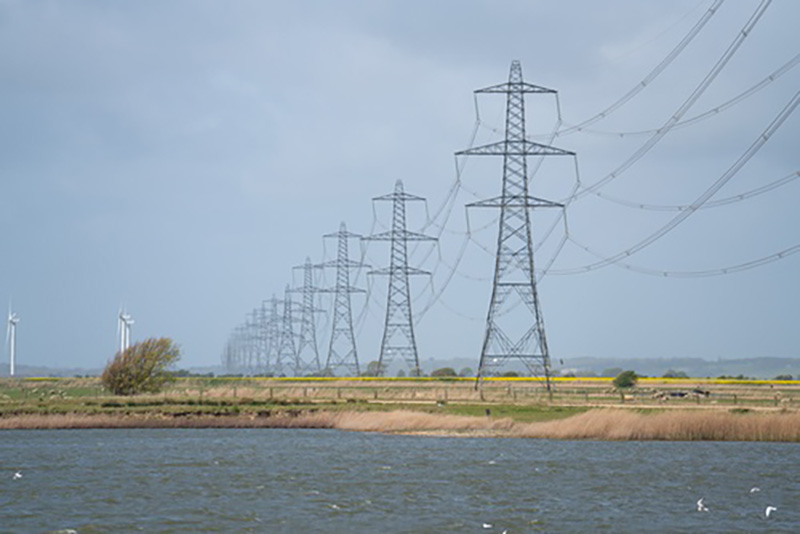 Electric pylons going across the land towards the sea and offshore wind farms