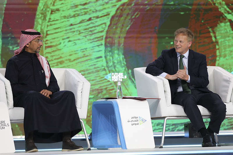 Two seated men in front of a green and brown backdrop