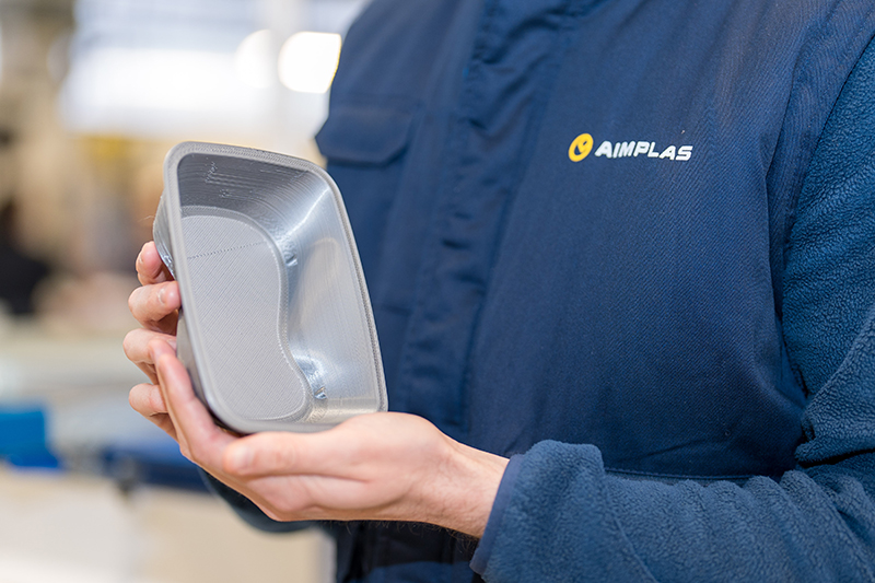 Employee from AIMPLAS branded uniform holding a plastic read meal container