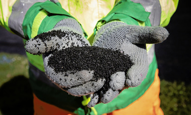 Close up of gloved hands holding a black powder.  The person is wearing safety clothing. 