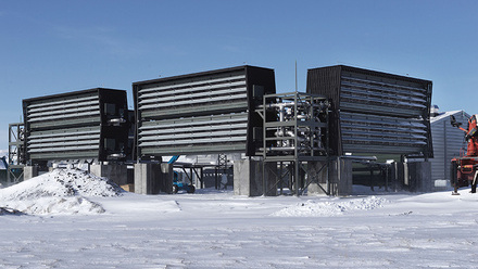 Climeworks Orca plant, Iceland. Three large black rectangular structures with horizontal, steel coloured bars. The ground is snow-covered.  