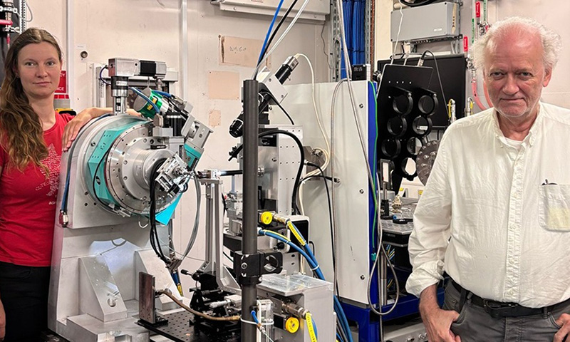 Female researcher in orange t-shirt wth machinery to her right and a male researcher in a white shirt to the far right
