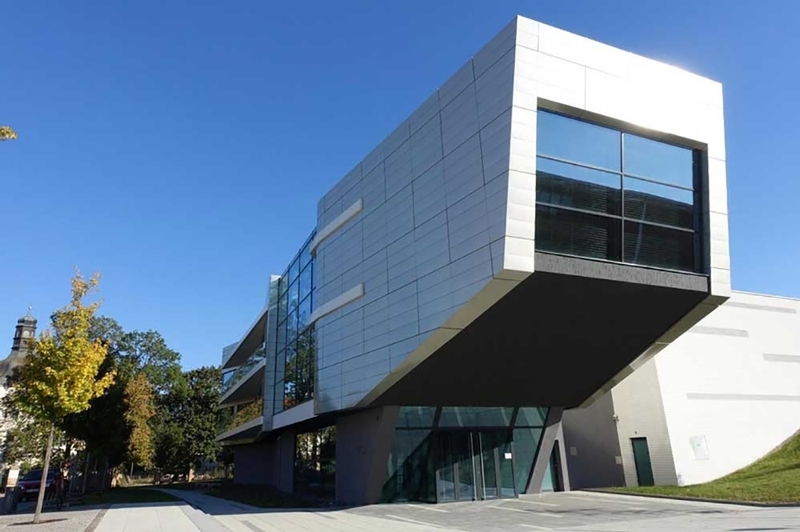 A white and black distinctively shaped building, the windows are tinted black and an are protrudes over the entrance