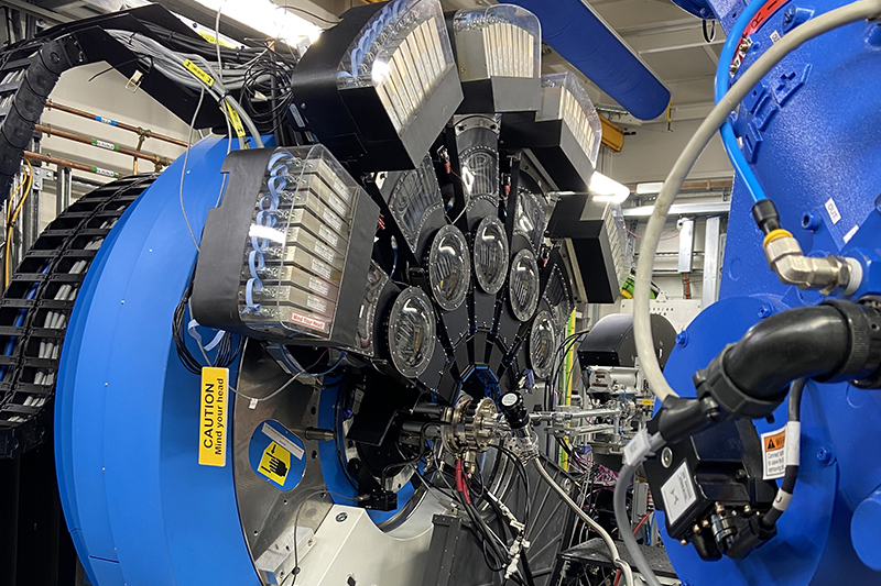 Large machine with like a giant circular container with electronics and equipment strapped to the outside with a single point of entry from a robot pushing a rod through into it