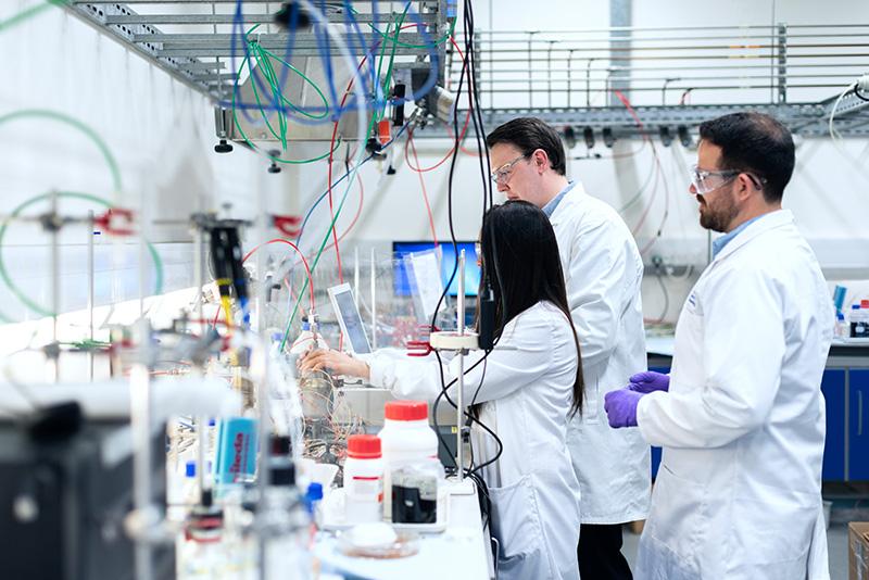 three scientists in white lab coats at a clutterd lab bench