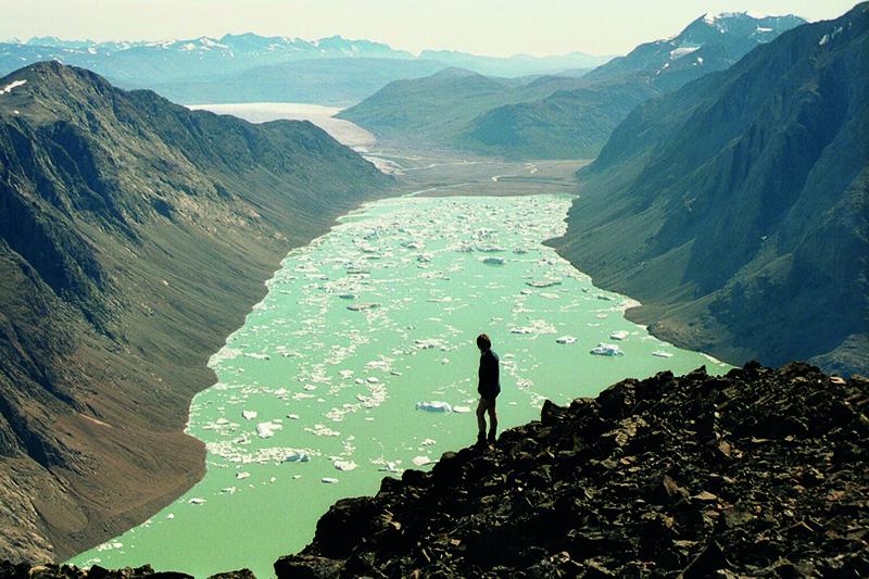 Silhouette of a man looking at a large valley filled with green water and ice floes