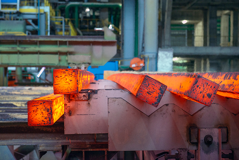 Red-hot steel beams made by an electric arc furnace rolling down a conveyor belt