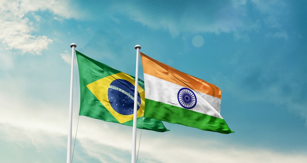Brazil and India flags are waving in a blue sky.