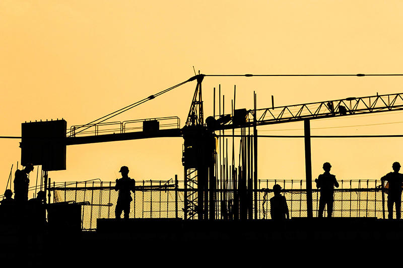 silhouette of construction workers on top of a building with a crane